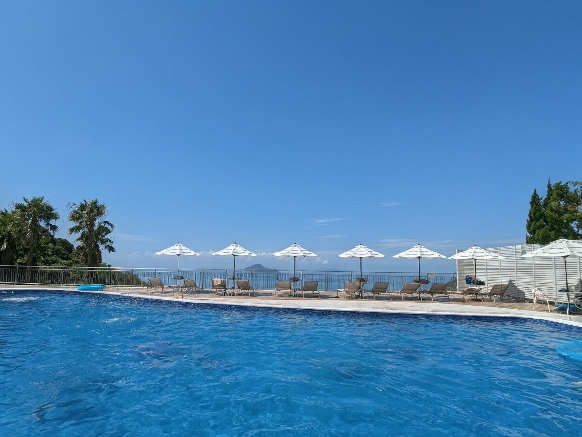 伊良湖オーシャンリゾートの屋外プール。白いパラソルとビーチチェアが並び、その向こうには伊勢湾の水平線が広がる開放的な景色。
