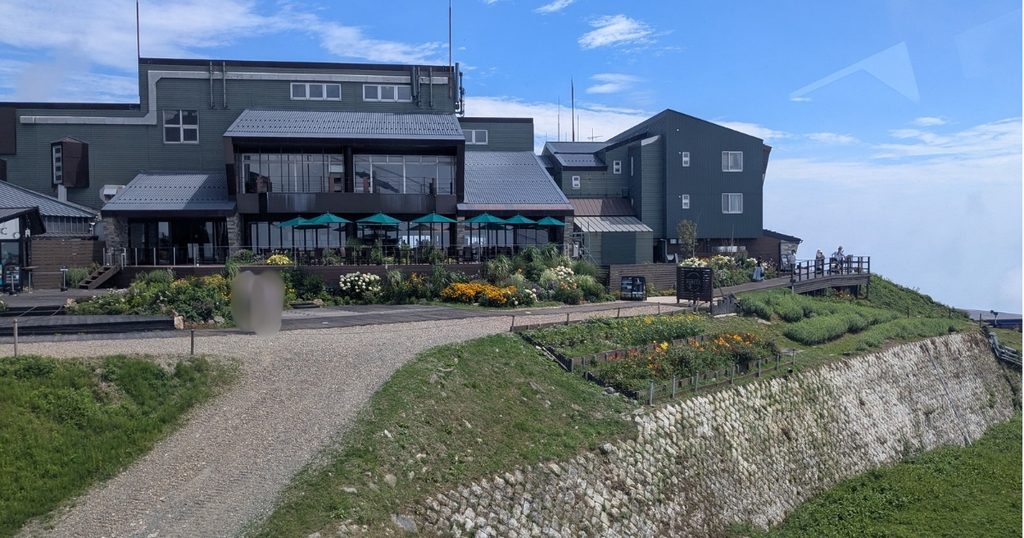 ロープウェイ山頂駅を降りてすぐの場所から見えるお花とびわ湖テラスのカフェ建物 (Biwako Terrace cafe building and flower  viewed from the ropeway summit station)
